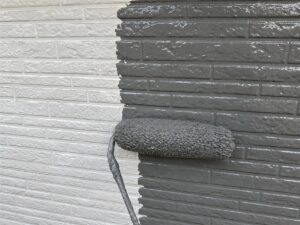 藤沢市の外壁の中塗りで下塗りの白の上にグレーの塗料を塗り進めている様子
